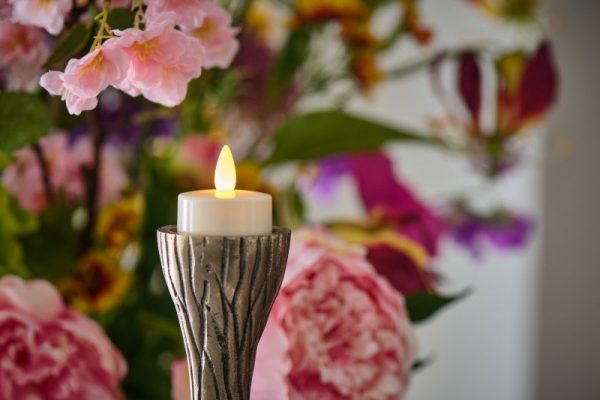 waxinelichtje met kaarsvet op houder op de achtergrond zijn roze bloemen te zien