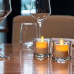 3 waxinelichtjes in glazen houder op tafel met wijnglazen in restaurant 