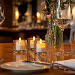 3 waxinelichtjes in glazen houder op tafel met wijnglazen in restaurant 