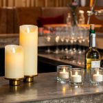 2 kaarsen met 3 waxinelichtjes op een bar met een vaas en flessen wijn