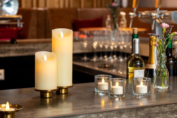 2 kaarsen met 3 waxinelichtjes op een bar met een vaas en flessen wijn