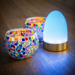 Een tafellamp van Dorsetto met blauw licht naast 2 gekleurde waxinehouders